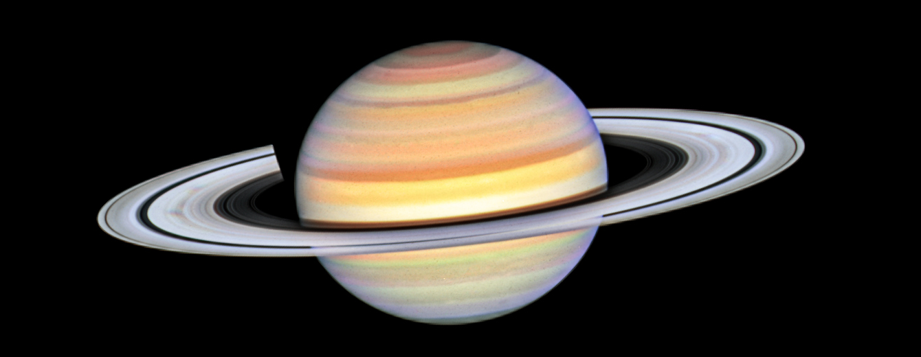 Saturn with bright white rings and multi-colored main sphere. Spoke features on the left and right sides of the rings appear like faint gray smudges against the rings' bright backdrop, about midway from the planet to the rings' outer edge. Above the rings plane, the planet's bands are shades of red, orange and yellow, with bright white nearer the equator. The background of space is black.