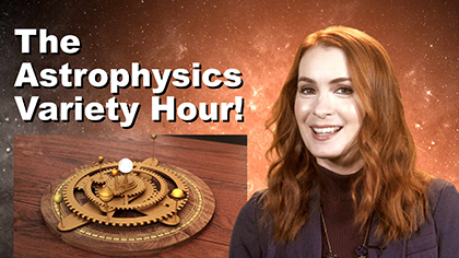 The video series title, "The Astrophysics Variety Hour!" sits in the upper-right quadrant. To the right, the show host, Felicia Day, smiles at the camera. A gold mechanical model of a solar system is under the title. Tiny bright stars and nebulous orange gas fill the background.