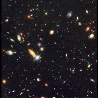On a grainy black background, dozens of galaxies of various shapes, sizes, and colors are scattered.