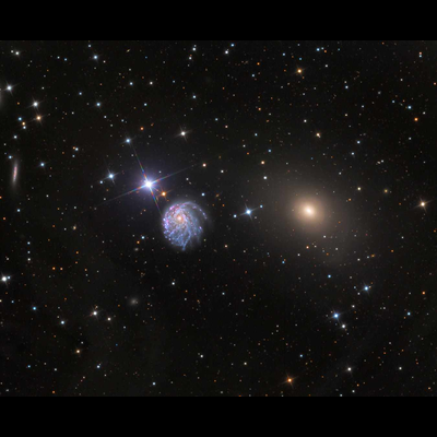 On a black, starry background are three bright objects in a horizontal row at the center: a bright star, a large spiral galaxy, and a smaller yellow galaxy.