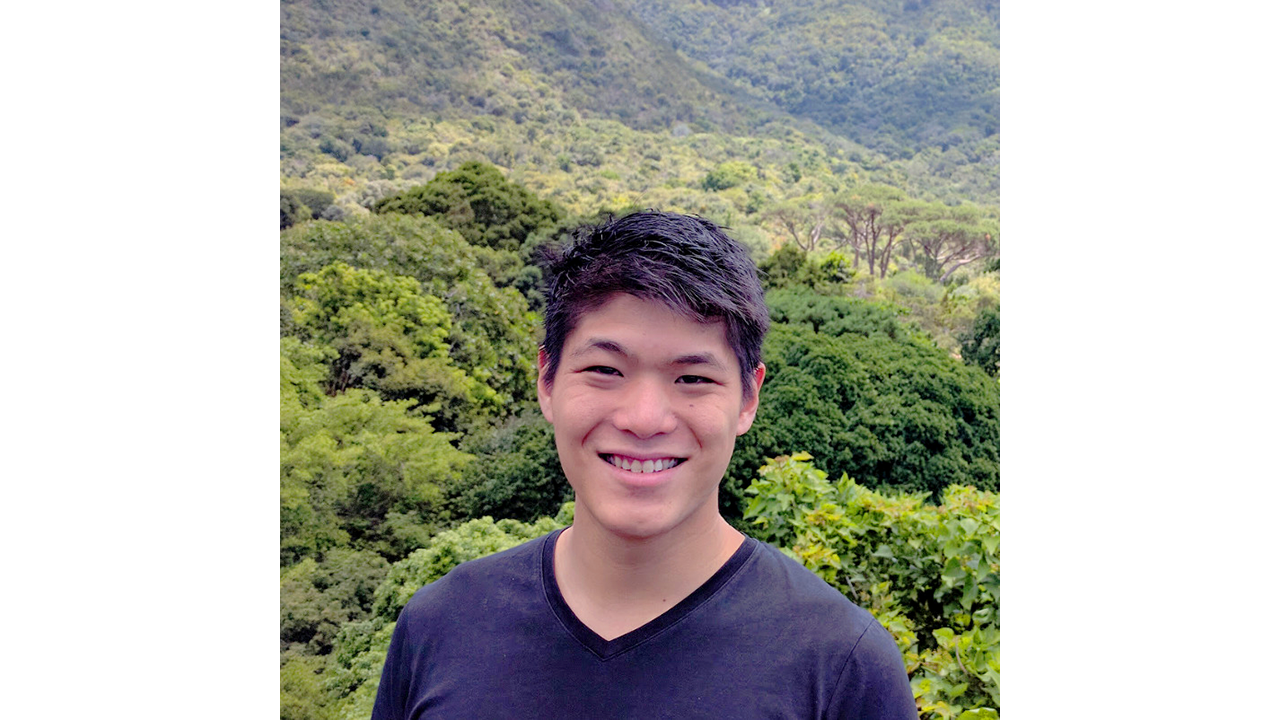 A man at image center with many green shrubs and trees in the background.