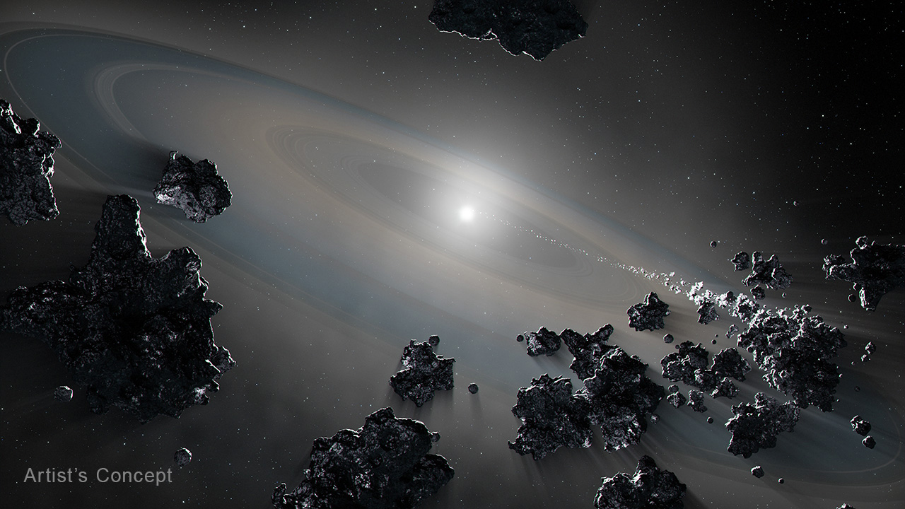 At image center is a small, white star against a gray background. It is surrounded by a large translucent disk with rings and gaps that extends from upper left to lower right. In the foreground, irregular chunky rocks are floating in space along the bottom of the frame. A stream of material extends from lower right toward the central star. The words, artist's concept are at lower left.