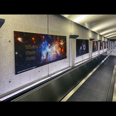 Closeup of Dulles airport hallway shows several large-scale James Webb Space Telescope images hung on the left side.
